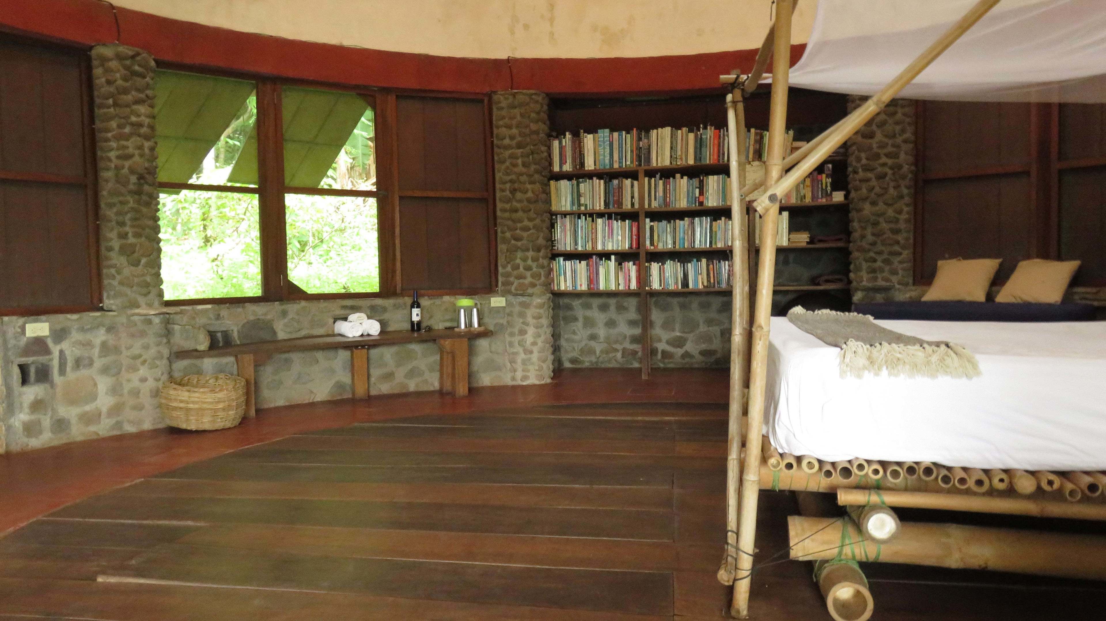 Quarto com cama, estante, janela e parede de pedra.