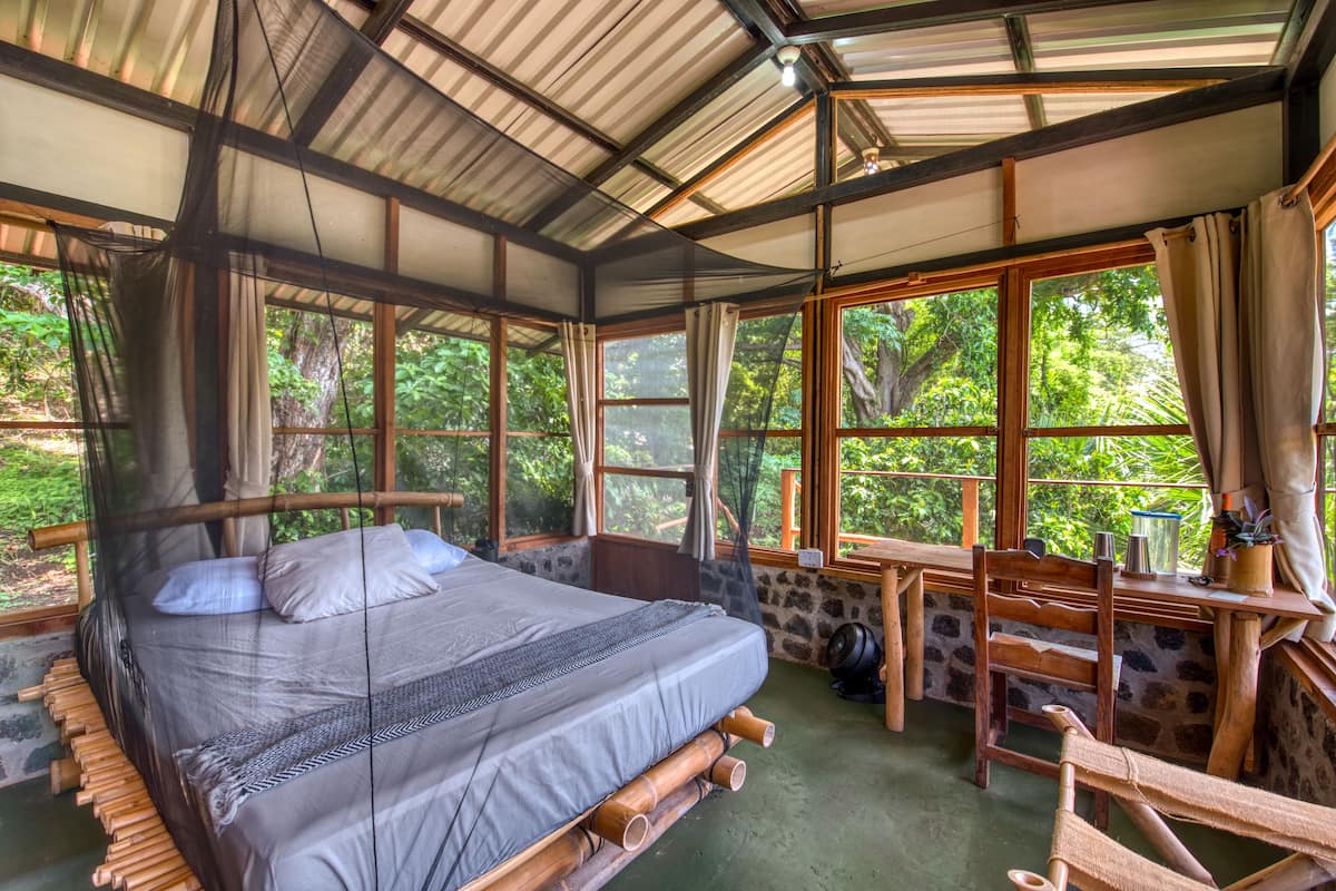 A room with a bed, wooden furniture, and large windows.