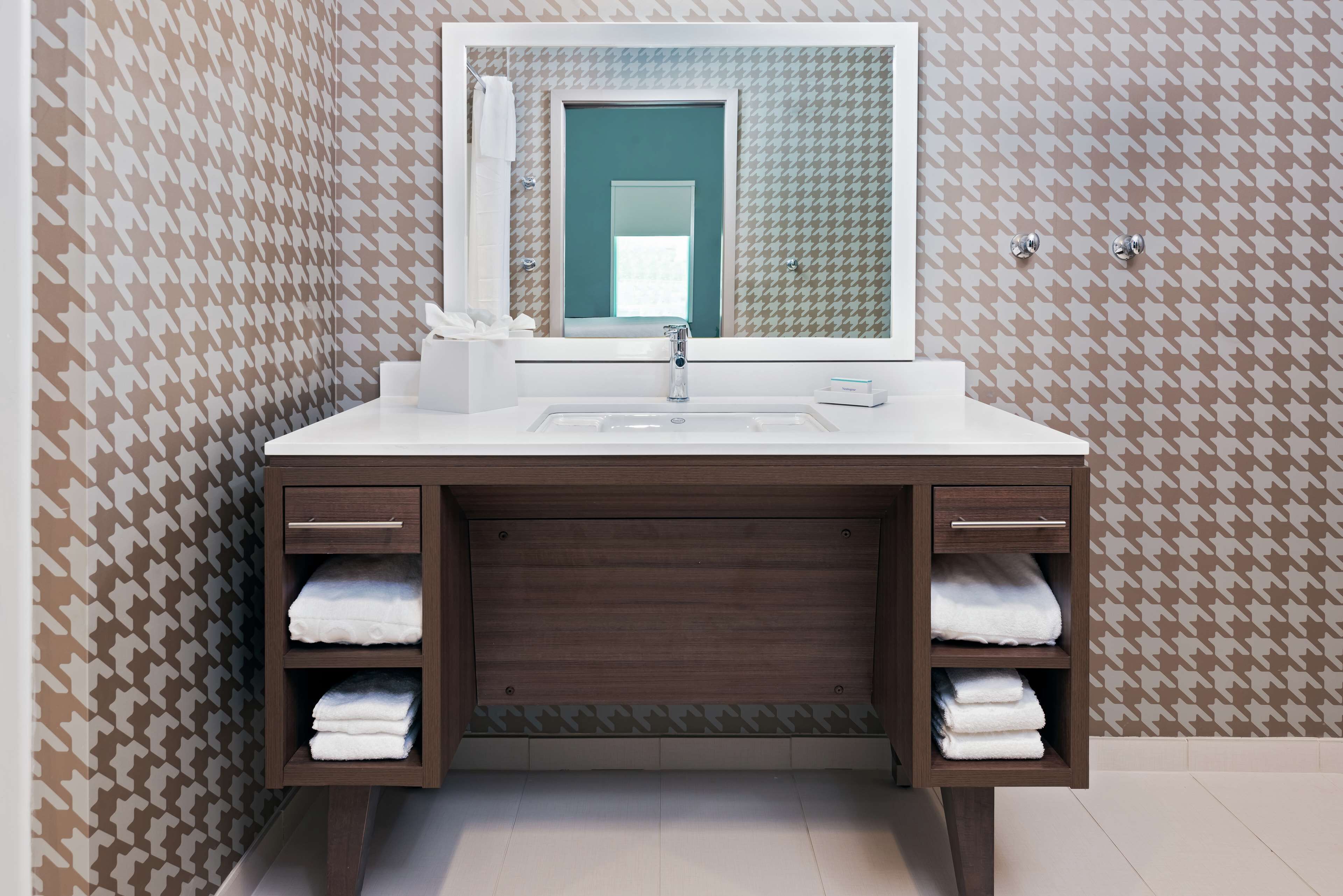 Un baño con un lavamanos blanco, un espejo y un mueble de tocador de madera con dos repisas para toallas.