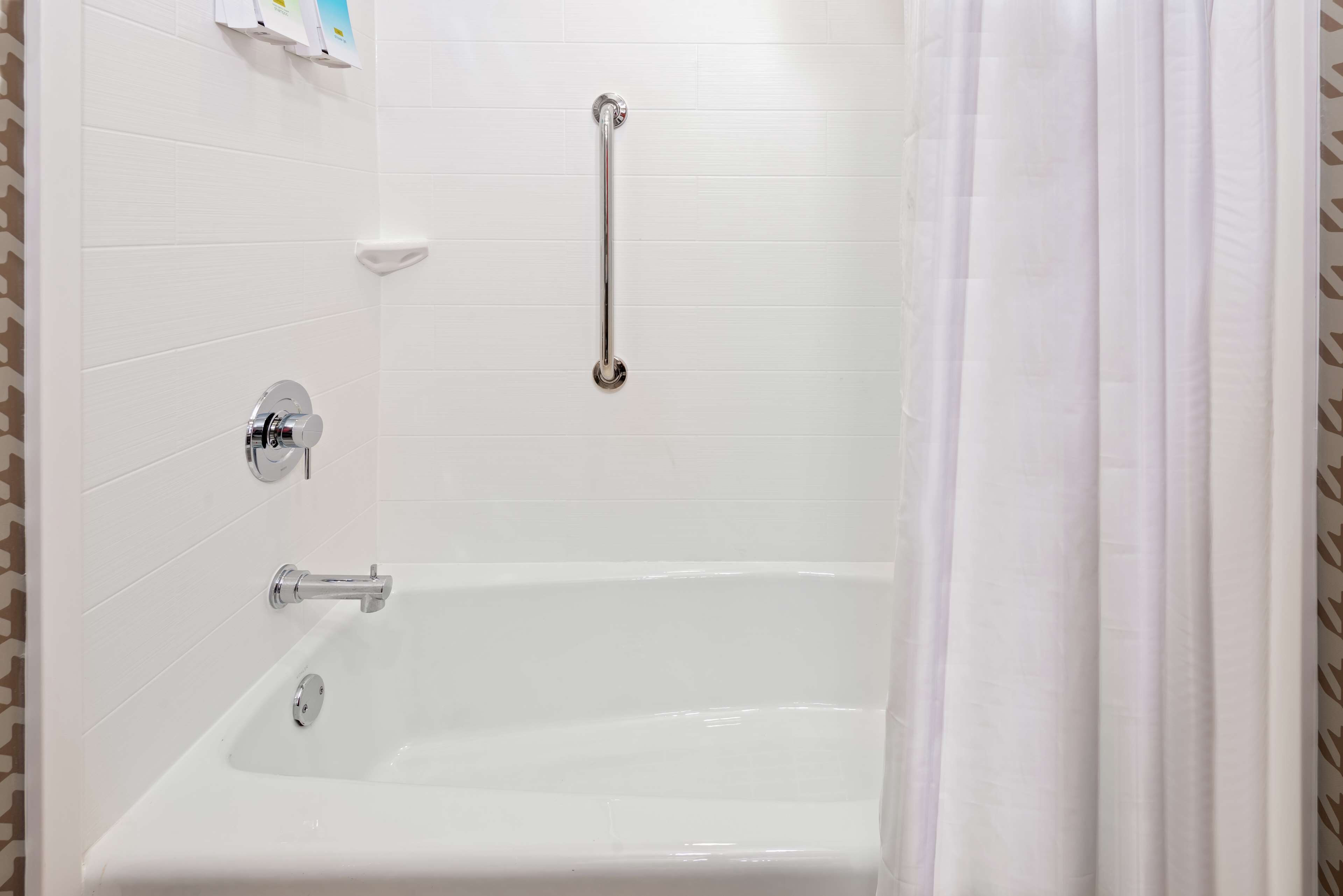 Une salle de bain avec une baignoire blanche, une douchette à main et une barre d’appui.