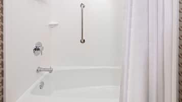 A bathroom with a white bathtub, a handheld showerhead, and a grab bar.