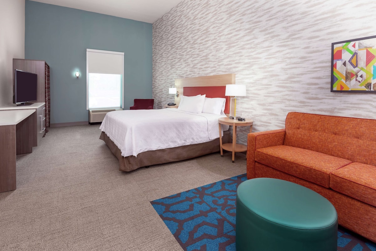 Une chambre d’hôtel avec un lit, une télévision, un bureau, un canapé et une peinture abstraite aux couleurs vives accrochée au mur.