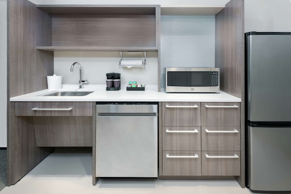 A compact kitchen with a dishwasher, microwave, and refrigerator. - Home2 Suites by Hilton Orlando Near Universal (Orlando)