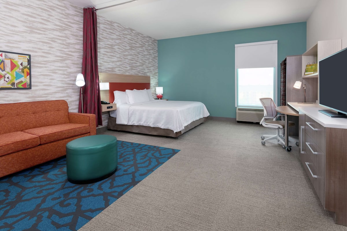 Une chambre d’hôtel comprenant un lit, un bureau, une chaise, un canapé, une télévision, une lampe et une fenêtre.