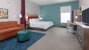 Habitación de hotel con cama, escritorio, silla, sofá, televisor, lámpara y ventana.