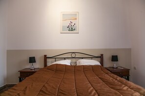 Een net opgemaakt bed met een bruine deken, twee nachtkastjes met lampen, en een ingelijst schilderij aan de muur.
