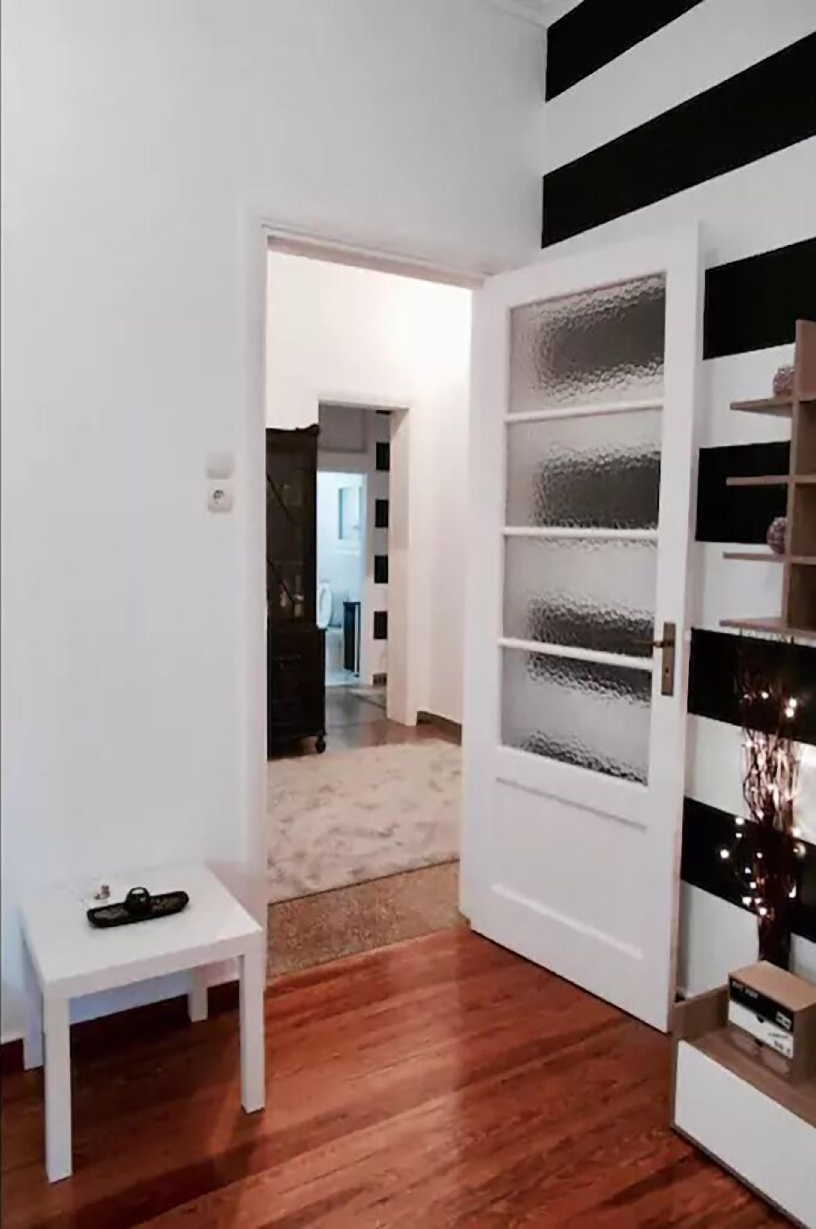 A hallway with a white door leading to a room, a small white table with a remote control, and a white shelving unit with glass doors.