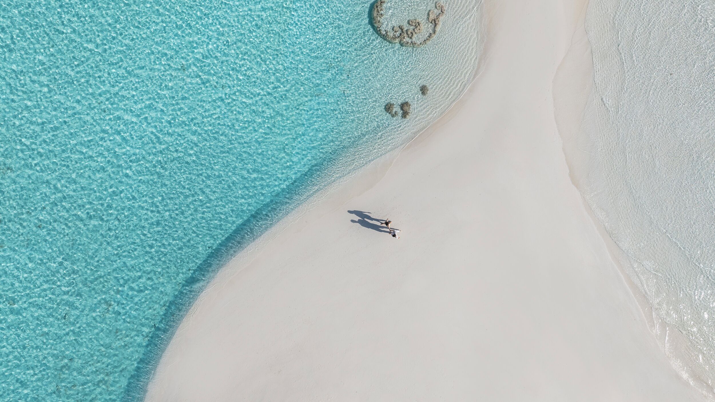 An aerial view of a beach with clear turquoise water and white sand.