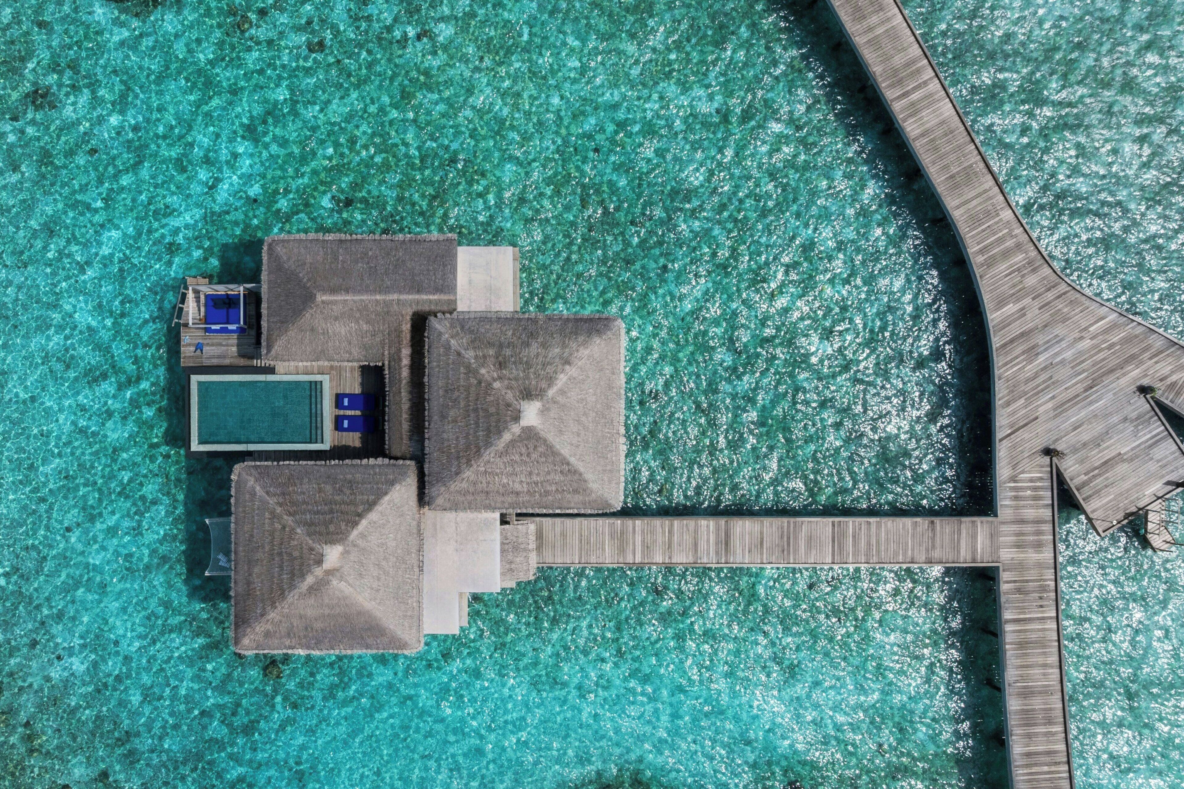An aerial view of a resort with overwater bungalows connected by a wooden walkway.