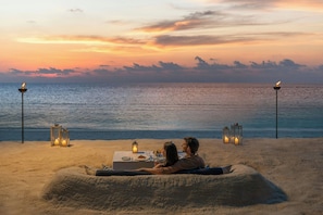 A couple dining on a beach with a view of the ocean and sunset. - The Halcyon Private Isles Maldives, Autograph Collection (Meradhoo)