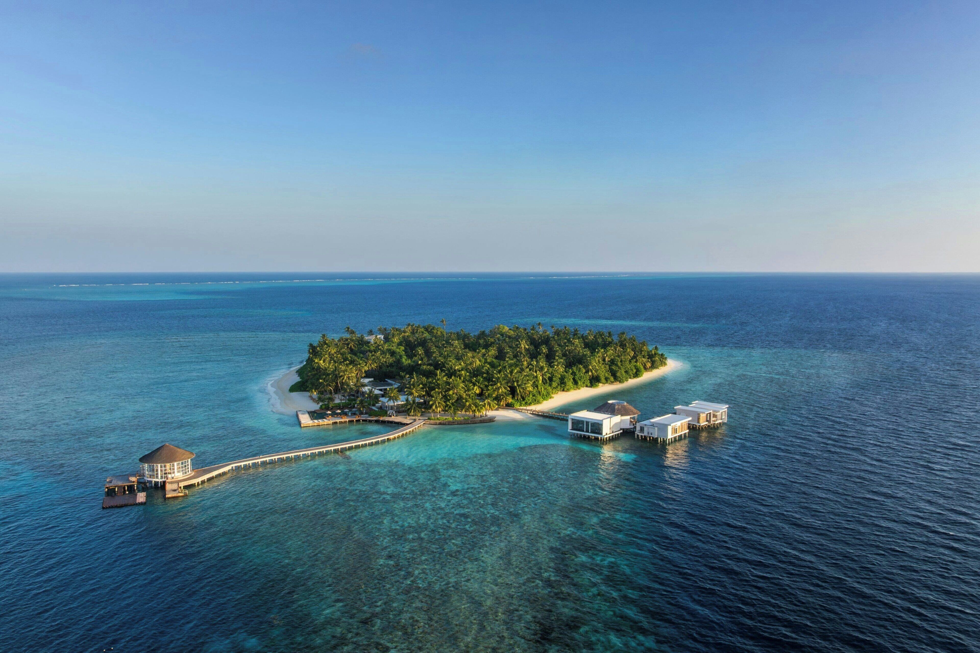 An island with a pier leading to overwater bungalows and a central building.