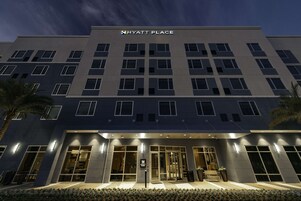 Un hotel moderno con un llamativo letrero de “HYATT PLACE”, grandes ventanales y una entrada bien iluminada.