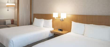 A hotel room with two beds, a bedside table with a clock, and a wall-mounted light fixture.