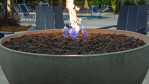 Un elemento decorativo con fuoco all'aperto, circondato da poltrone lounge e palme.