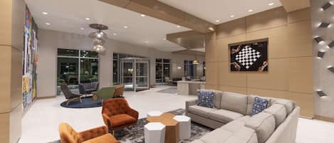 A modern lobby with a sofa, armchairs, and a coffee table. There is a large window and a wall-mounted artwork.