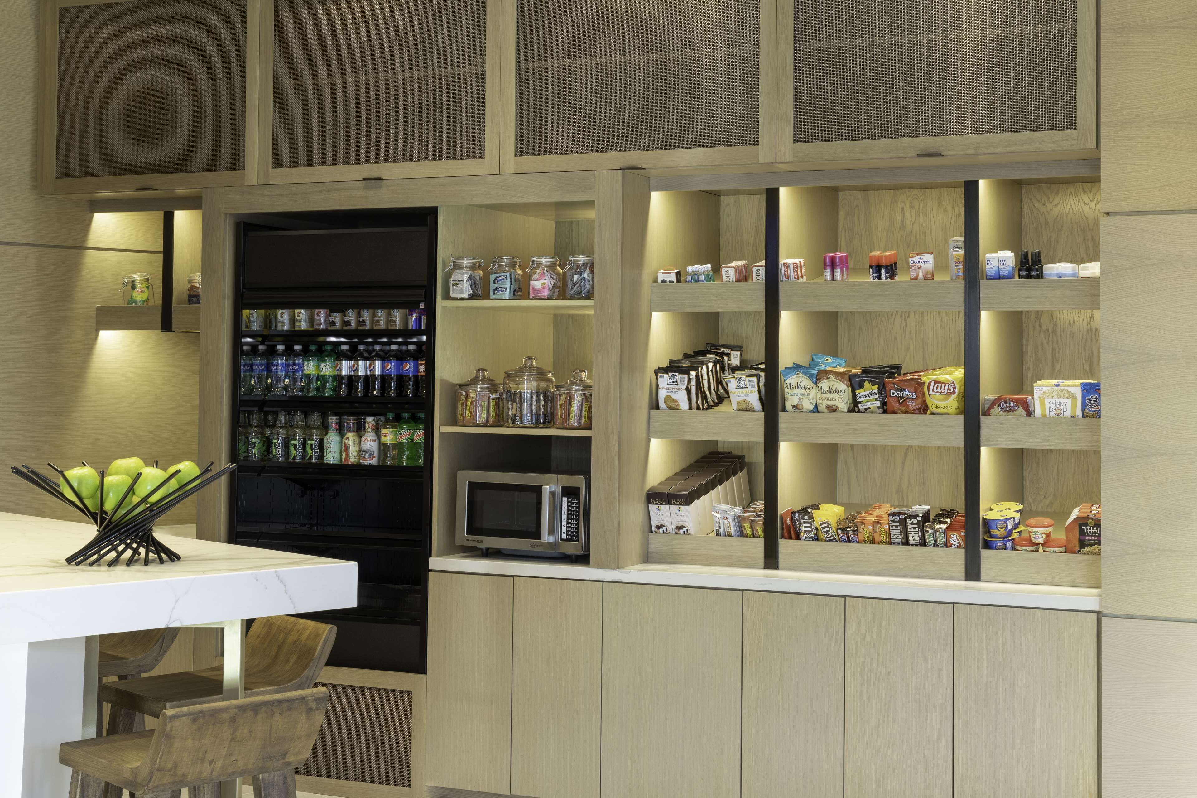 A kitchen with a microwave, refrigerator, and various food items on shelves.