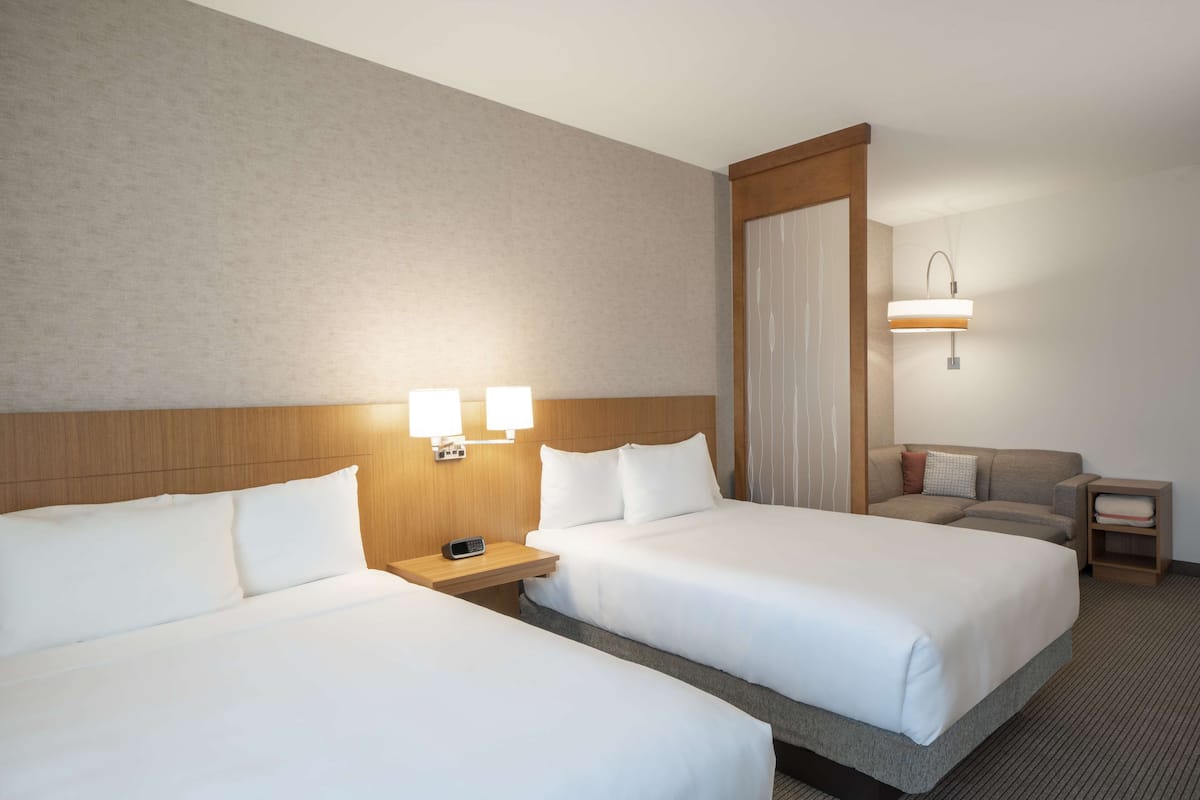 Habitación de hotel con dos camas, una mesita de noche con teléfono, una lámpara y un sofá.