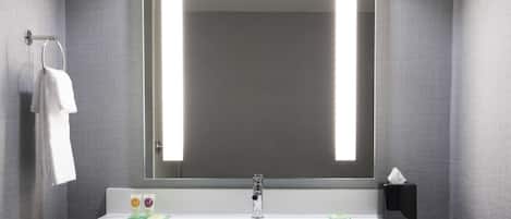 A modern bathroom with a large mirror, white sink, and wooden vanity.