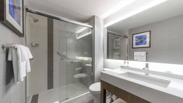 Un baño moderno con ducha de vidrio, inodoro y lavamanos con espejo.