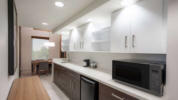 A modern kitchen with white cabinets, a black microwave, and a wooden dining table.