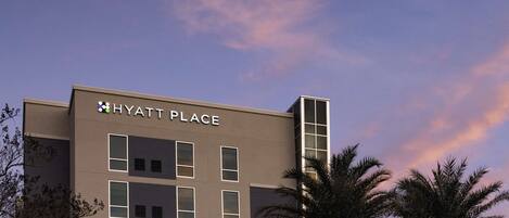 A modern building with the sign "HYATT PLACE" on the facade, featuring a symmetrical window layout and a vertical accent on the right side.