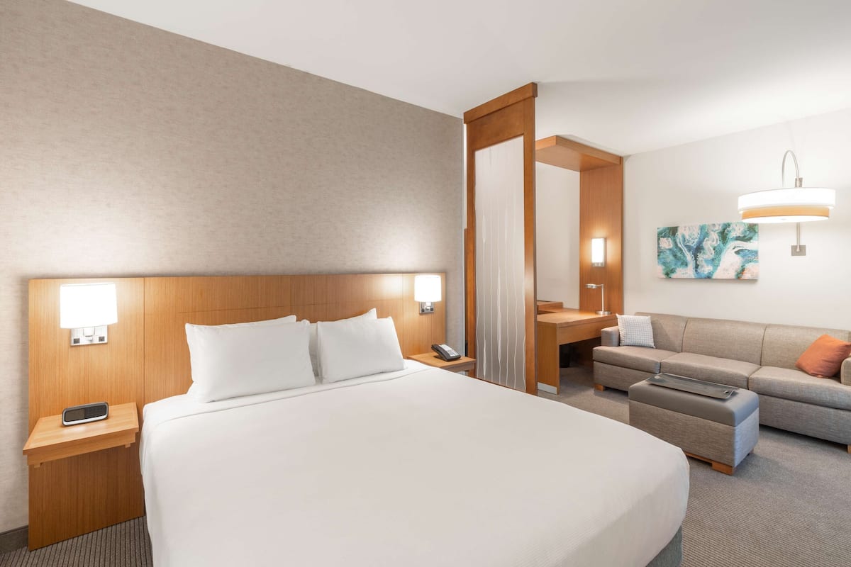 Habitación de hotel con una cama grande, un escritorio, un sofá y un baño visible a través de una puerta abierta.