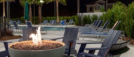 A poolside area with lounge chairs, a fire pit, and a pool.