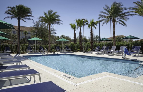 A swimming pool with lounge chairs and umbrellas, surrounded by palm trees and a building in the background. - Hyatt Place Sandestin at Grand Boulevard (Miramar Beach)