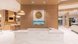 Una cucina moderna con isola centrale, illuminazione a sospensione e un quadro appeso raffigurante una spiaggia.