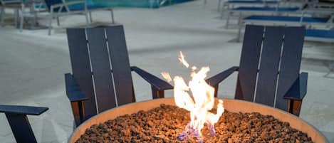 Un área junto a la piscina con una fogata y sillones de descanso.