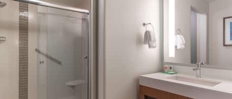 A modern bathroom with a glass-enclosed shower, a white sink with a mirror, and a wooden vanity.