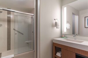Een moderne badkamer met een douche met glazen wand, een witte wastafel met spiegel en een houten opbergmeubel.