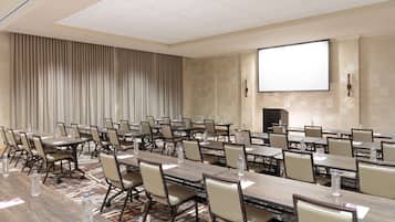 A conference room with multiple tables and chairs, equipped with water bottles and presentation screens.
