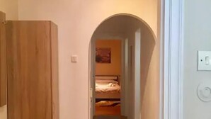A narrow hallway with a wooden wardrobe on the left, a carpeted floor, and a bed visible through an arched doorway in the distance. - Acropolis modern house (Athens)