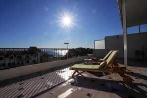 Terraza en la azotea iluminada por el sol con vistas despejadas al mar, una tumbona y una mesa.