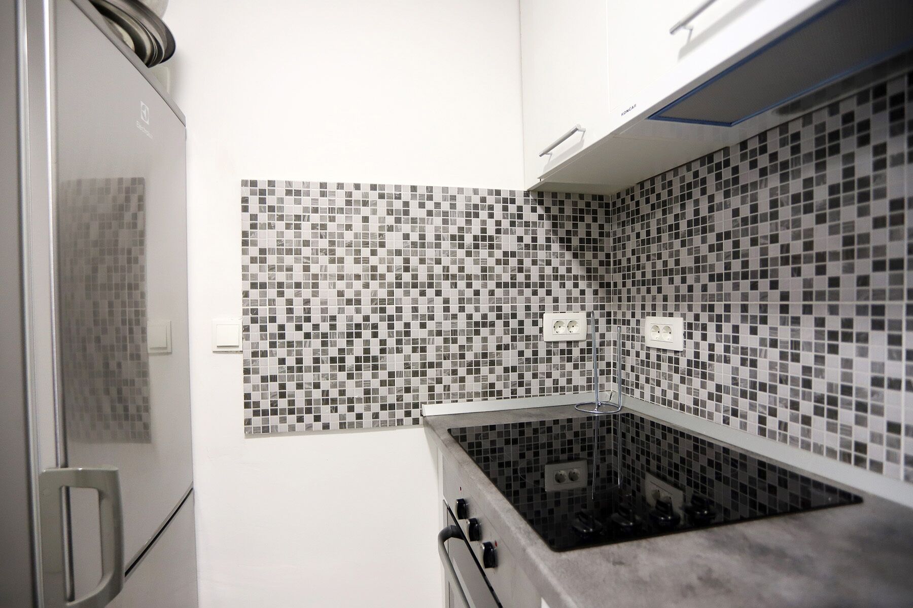 A kitchen with a modern design, featuring a black and white mosaic backsplash, stainless steel appliances, and a built-in oven.