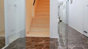 Un pasillo moderno con suelo de mármol, una escalera y paredes blancas.