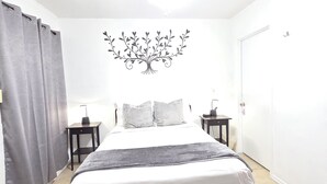 A bedroom with a bed, a nightstand, a wall decoration, a door, and a curtain. - Williams AZ Hostel (Williams)