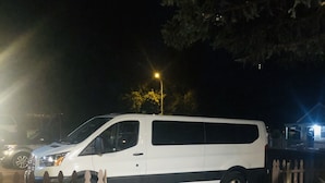A white van parked in front of a wooden fence with a paved driveway leading to a house. - Williams AZ Hostel (Williams)