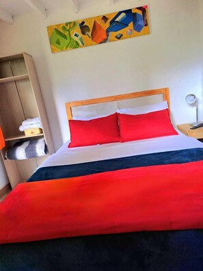 A bed with red and white bedding, a wooden headboard, and a painting above it. - Hotel Marrokos (Guarne)