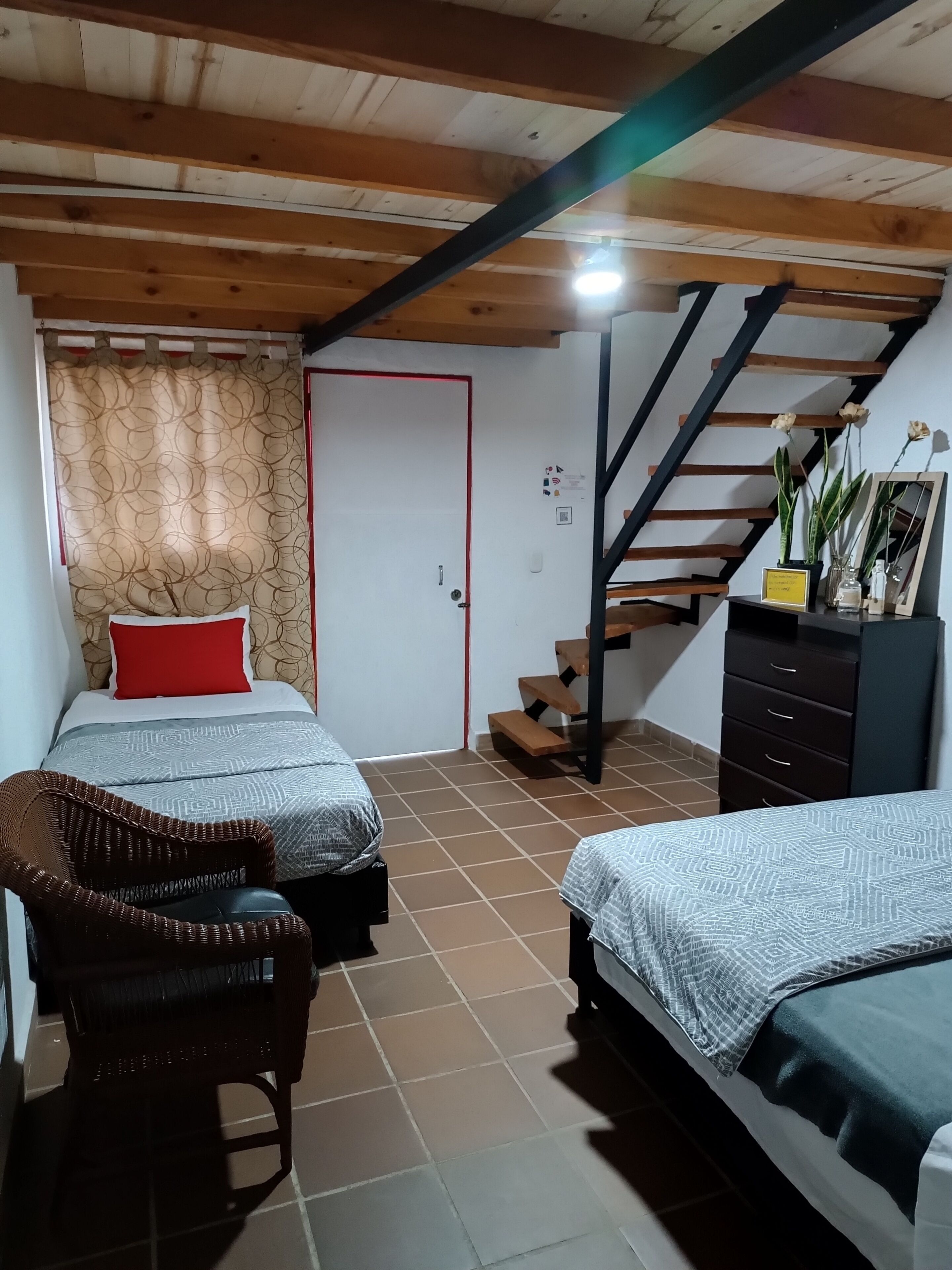 A bedroom with two beds, a wooden staircase, a dresser, and a chair.