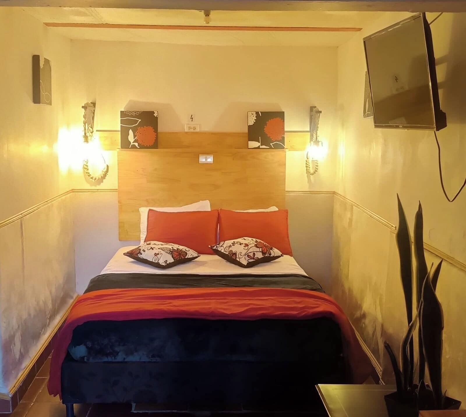 Ein Hotelzimmer mit einem Bett, zwei Wandleuchten, einem Flachbildfernseher und einem Holzkopfende.