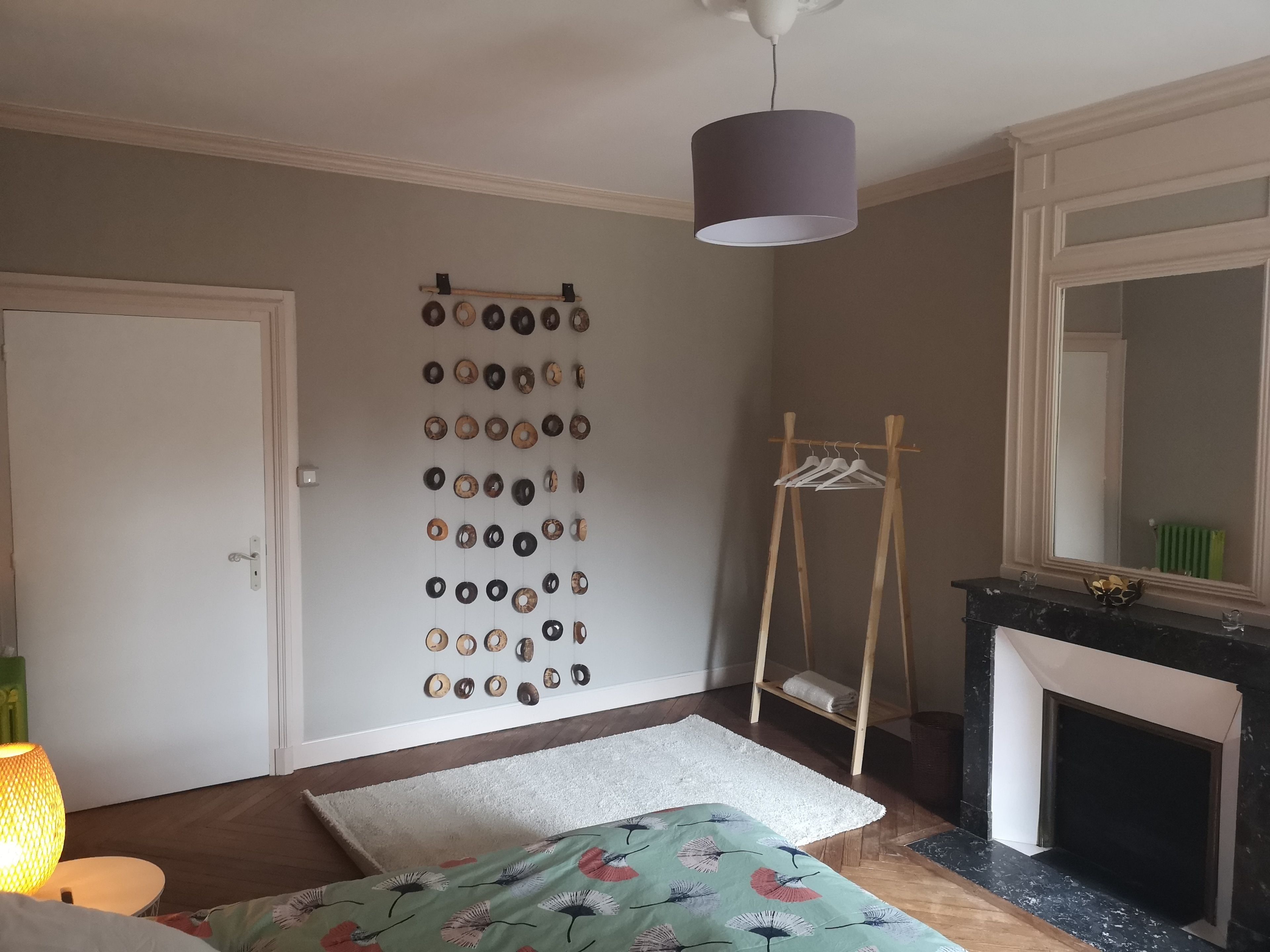 A bedroom with a bed, a hanging light fixture, a mirror, and a wall-mounted coat rack.