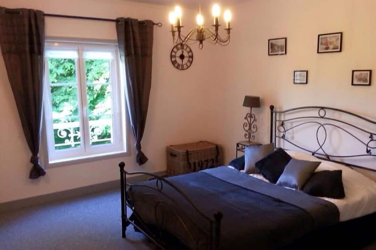 A bedroom with a bed, a window with curtains, a wall clock, and framed pictures.