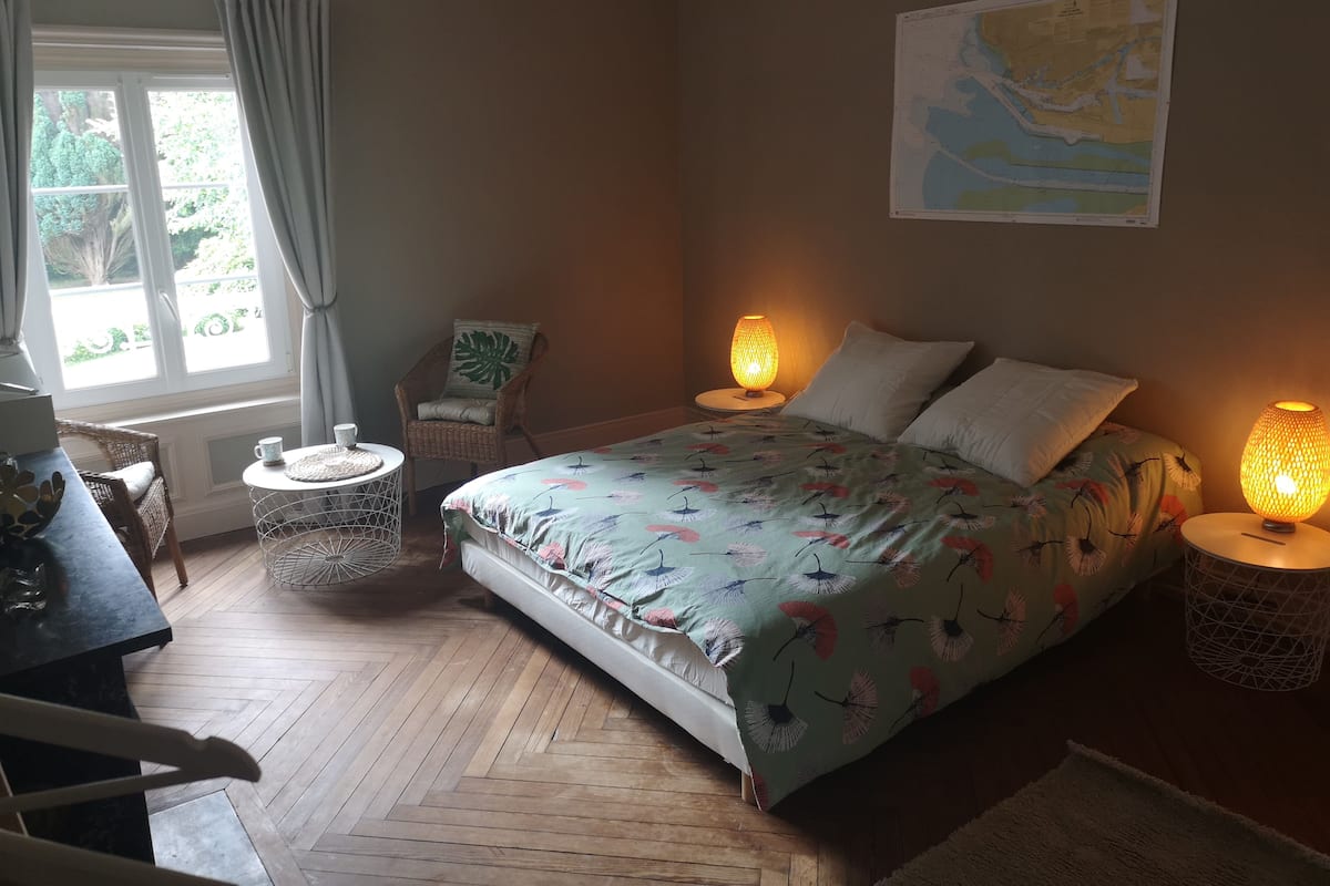 A bedroom with a bed, two bedside lamps, a chair, a small table, and a map on the wall.