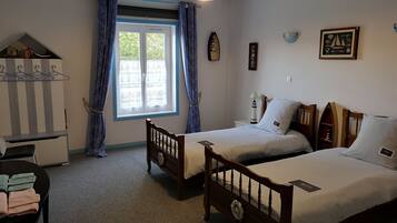 Una habitación con dos camas individuales, una mesita, una silla, un ventanal con cortinas y una lámpara.