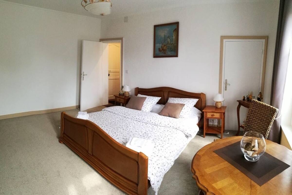 A bedroom with a wooden bed, a bedside table with a lamp, a chair, and a painting on the wall.