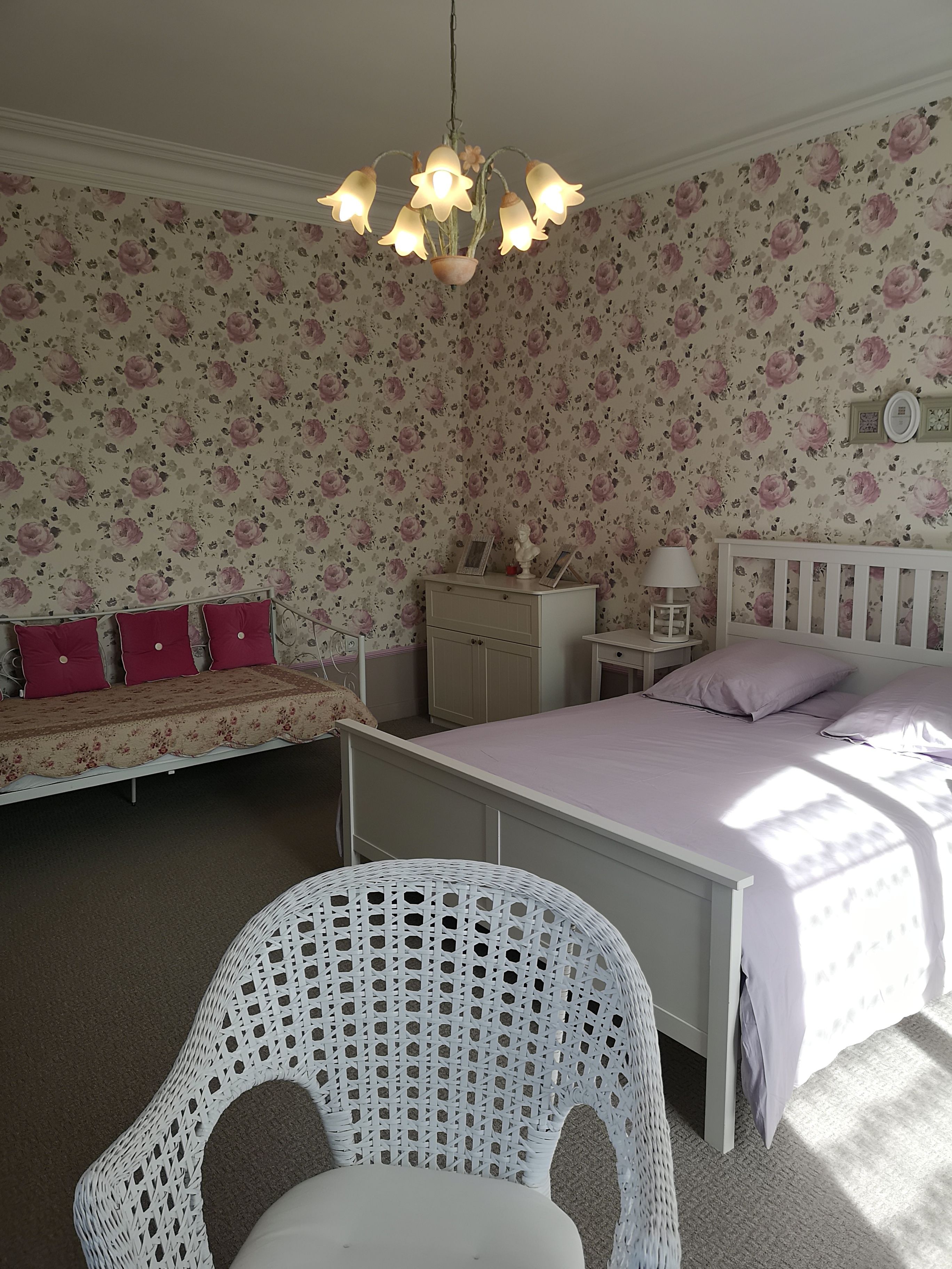 Un dormitorio con cama, mesita de noche, cómoda, silla y un reloj de pared.