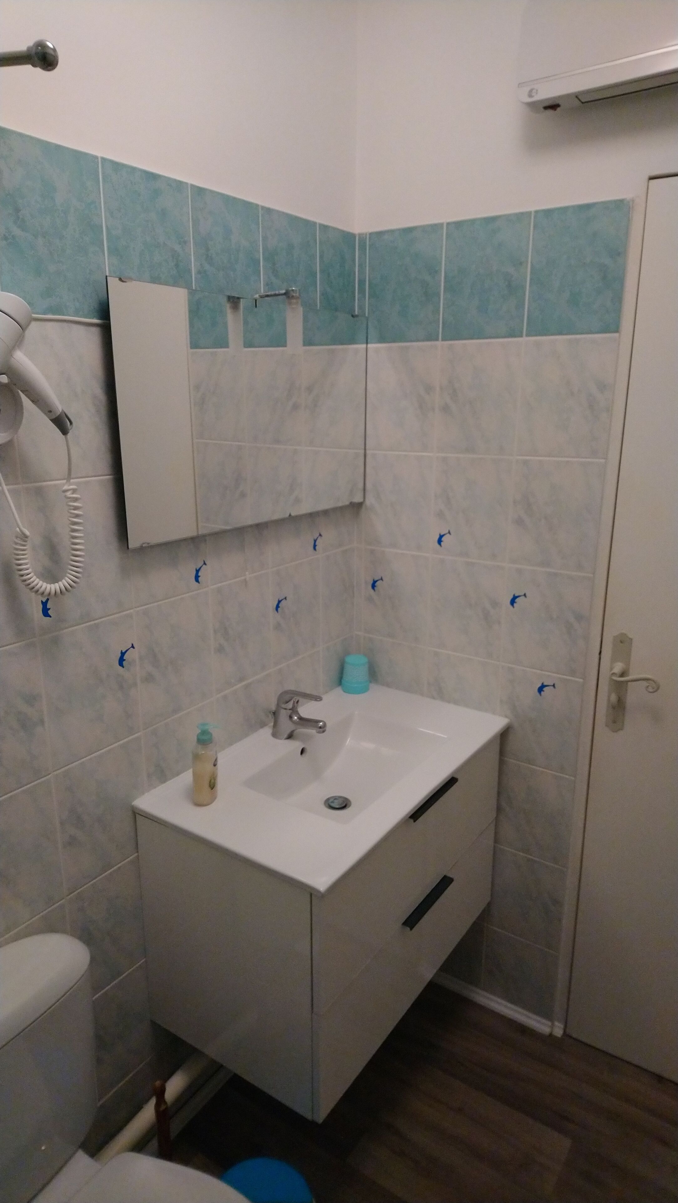 Un baño con lavamanos blanco, espejo y secador de pelo en la pared.