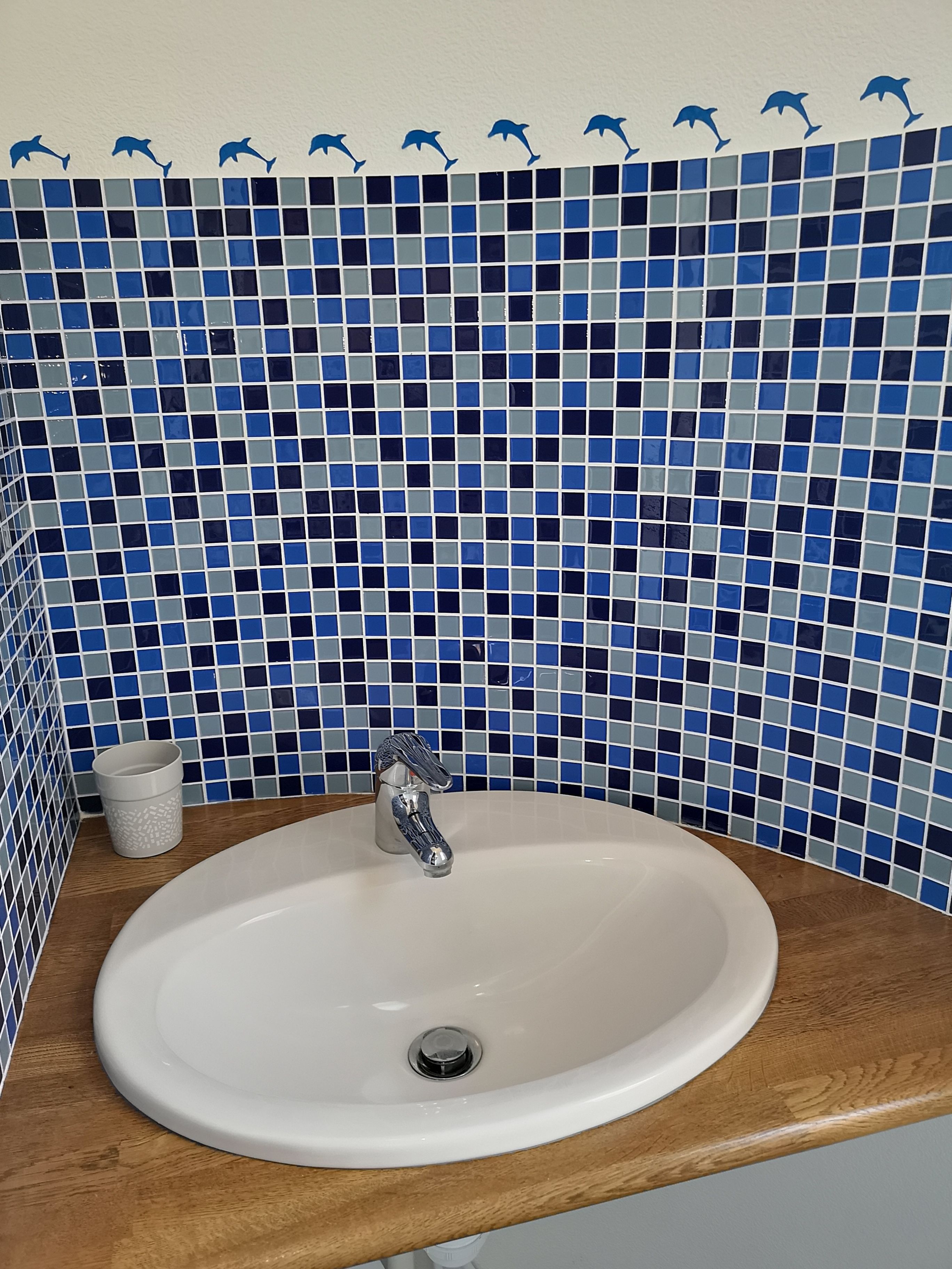A bathroom with a white sink, a silver faucet, and a tiled backsplash featuring blue and gray tiles.